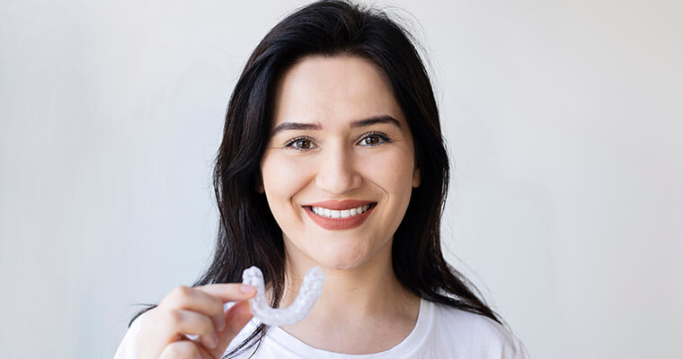 Dark-haired, smiling woman holding her clear aligner, demonstrating that it's removable.